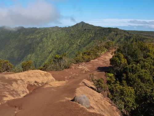 A scenic view of a rugged mountain trail surrounded by lush green hills under a clear blue sky.