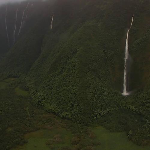 Aerial view of lush green mountains with multiple waterfalls cascading down the cliffs.