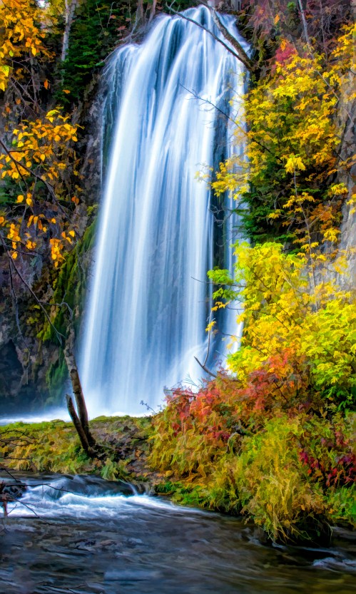 A vibrant waterfall cascades down rocky cliffs, surrounded by colorful autumn foliage and a serene river below.
