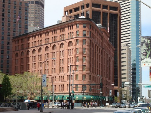 Historic red brick building on a city street, surrounded by modern skyscrapers and greenery.