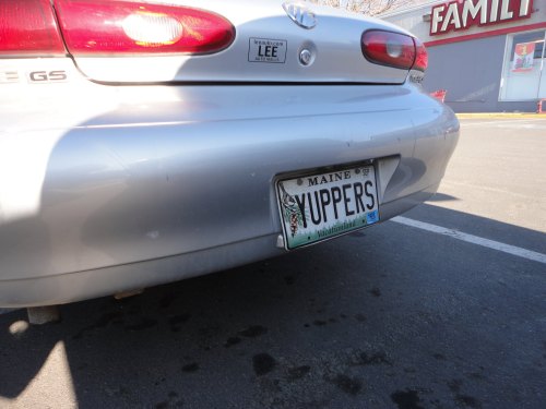 A silver car with a Maine license plate reading "YUPPERS" parked in a lot near a store.