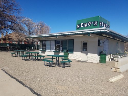 A small food stand named "Nemo's" with outdoor seating and a clear blue sky in the background.