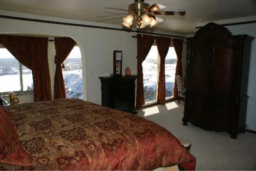 Cozy bedroom with a large bed, dark wood furniture, and windows offering a scenic view.
