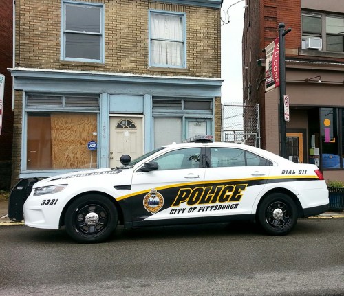 A Pittsburgh police car parked in front of a boarded-up building on a city street.