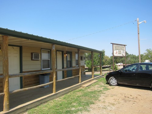 A small, rustic building with a porch and a sign reading "Briarwood Inn," alongside a parked black car.