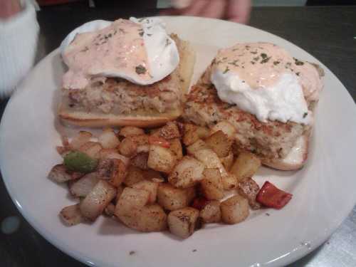 Two poached egg sandwiches on toasted bread with a creamy sauce, served with seasoned diced potatoes on the side.