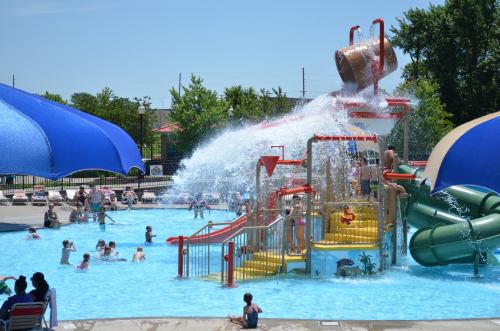 A vibrant water park scene with a large slide, splash pad, and children playing in a pool under sunny skies.