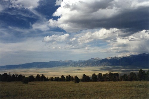 A vast landscape featuring rolling hills, mountains in the distance, and a dramatic sky filled with clouds.
