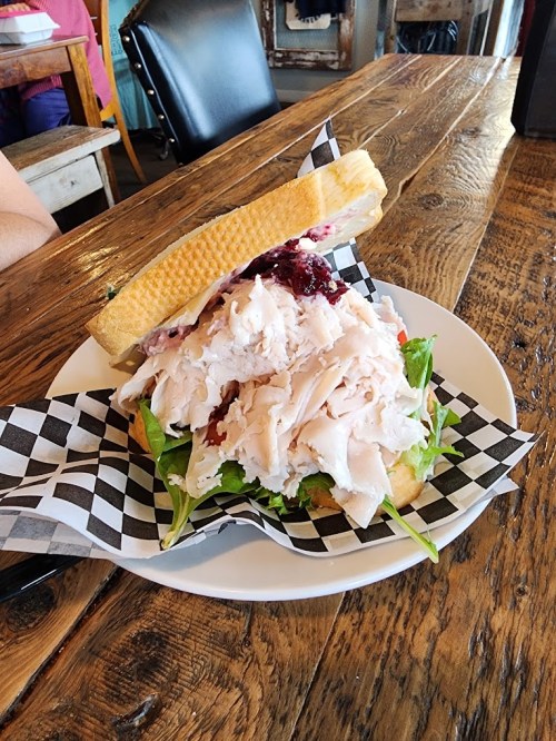 A large sandwich stacked with turkey, lettuce, and cranberry sauce on a checkered plate, set on a wooden table.