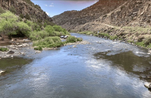 A serene river flows through a rocky landscape, surrounded by lush greenery and steep hills.