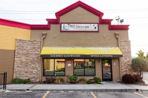 Exterior of "Deli George" featuring a colorful sign, yellow awning, and a landscaped entrance.