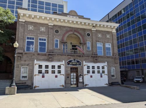 Historic building with a museum sign, large garage doors, and an American flag, surrounded by modern architecture.
