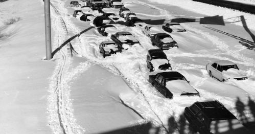 A snow-covered highway with stranded cars buried in deep snow, creating a scene of winter chaos.