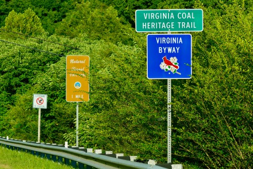 Signs for Virginia Coal Heritage Trail and Virginia Byway along a roadside, surrounded by greenery.