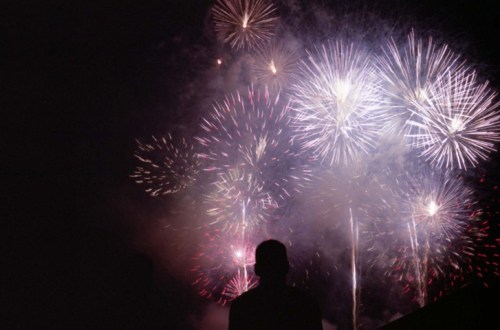 A silhouette of a person watching colorful fireworks explode in the night sky.