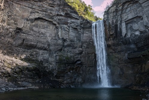 A majestic waterfall cascading down rocky cliffs into a serene pool below, surrounded by lush greenery.