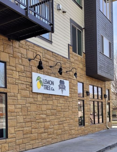 A stone building exterior featuring a sign for "Lemon Tree Co." with a lemon graphic and decorative lighting.