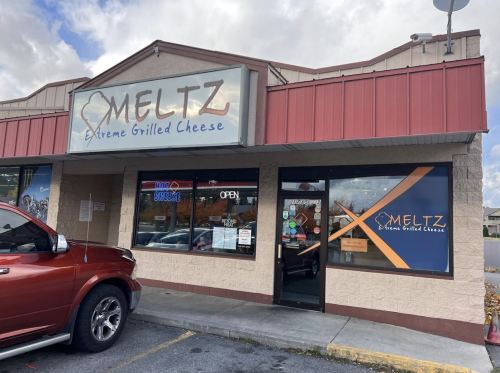 Exterior of Meltz Extreme Grilled Cheese restaurant, featuring a red and beige facade with an open sign and large windows.