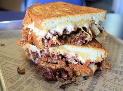 A stacked grilled cheese sandwich with crispy edges, melted cheese, and a savory filling on a paper-lined tray.