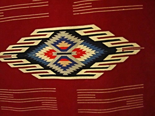 Colorful geometric pattern featuring blue, red, and cream designs on a red background.