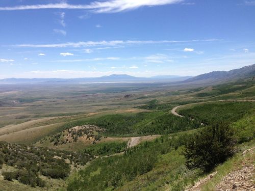 A panoramic view of rolling green hills and a vast valley under a blue sky with scattered clouds.