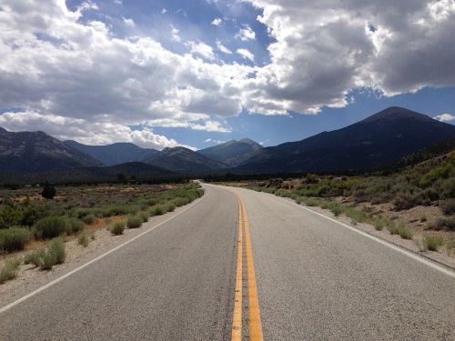 A winding road stretches through a mountainous landscape under a partly cloudy sky.