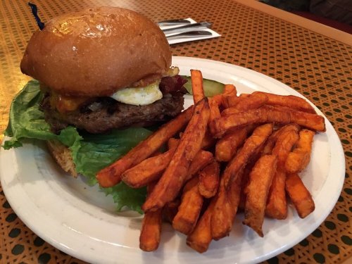 A juicy burger with lettuce, bacon, and a fried egg, served with a side of crispy sweet potato fries.