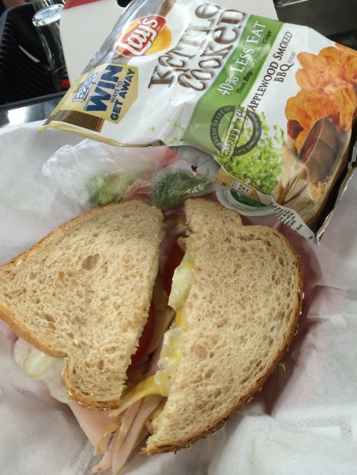 A sandwich with turkey, lettuce, tomato, and mayonnaise, alongside a bag of Lay's Kettle Cooked chips.