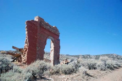 A weathered brick archway stands alone in a barren landscape under a clear blue sky.