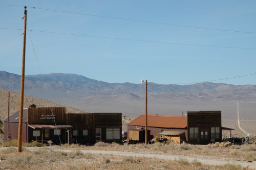 Abandoned buildings in a desert landscape with mountains in the background and a clear blue sky.