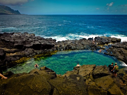 A natural rock pool by the ocean, with people swimming and enjoying the scenic coastal view.