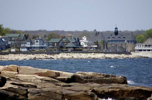 Coastal view featuring rocky shoreline and a row of elegant homes along the water's edge on a clear day.