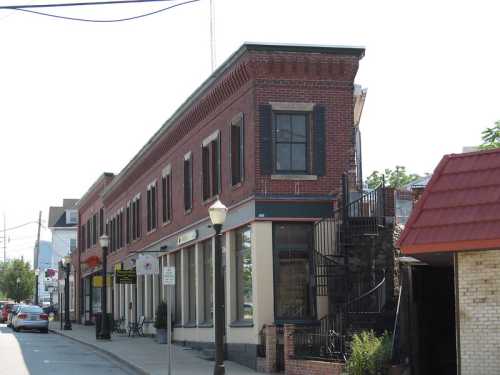 A brick building with large windows and a staircase, located on a street with parked cars and streetlights.