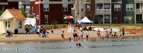 A beach area with families and children playing in the water, surrounded by apartment buildings and a lifeguard station.