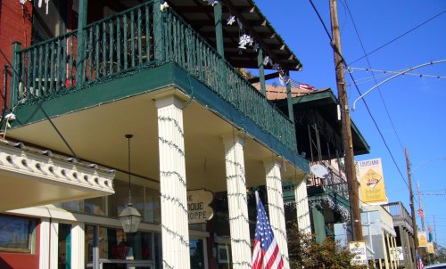 A charming storefront with a green balcony, decorated with lights, and an American flag, set against a clear blue sky.