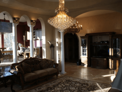 Luxurious living room with elegant furniture, chandeliers, and arched columns, bathed in warm sunlight.