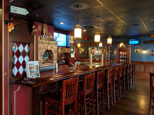 A cozy bar interior with wooden stools, a stone fireplace, and TVs, featuring a warm, inviting atmosphere.