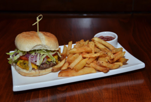 A juicy burger with lettuce, tomato, and pickles, served with crispy fries and a small cup of ketchup on a white plate.