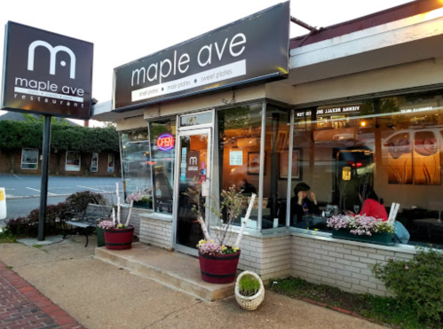 Exterior of Maple Ave restaurant with a sign, open window, and outdoor seating, surrounded by flowers and greenery.