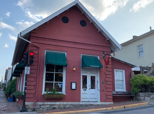 A red brick restaurant with green awnings, white doors, and a traffic light in front, set against a blue sky.