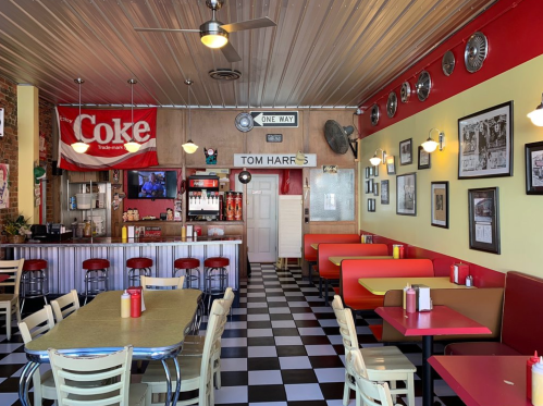 A retro diner interior with red and yellow seating, checkered floor, vintage decor, and a soda fountain.