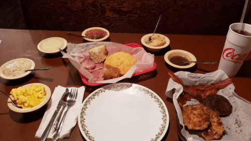 A table set with various dishes, including meats, cornbread, sides, and a drink, ready for a hearty meal.