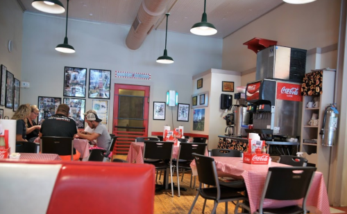 A cozy diner interior with checkered tablecloths, vintage decor, and a Coca-Cola machine in the corner.