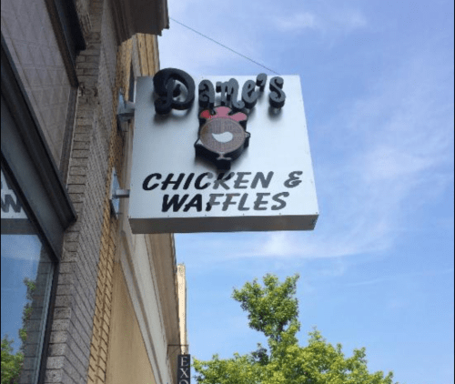 Sign for Dame's Chicken & Waffles, featuring a cartoon chicken logo, against a clear blue sky.