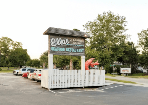 Sign for Ella's Seafood Restaurant in Calabash, featuring a large lobster sculpture and surrounded by parked cars.
