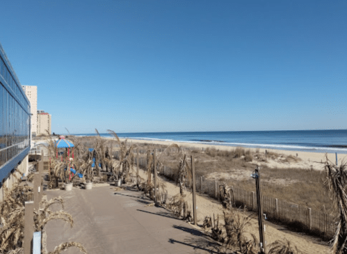 A clear blue sky over a sandy beach with a boardwalk and playground in the foreground.