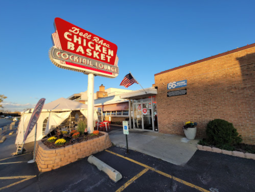 Exterior of Dell Rhea's Chicken Basket with a retro sign, featuring a cocktail lounge and an American flag.