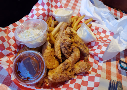 A basket of fried chicken tenders, fries, coleslaw, and dipping sauces on a red and white checkered paper.