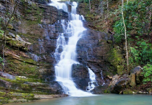 A serene waterfall cascading down rocky cliffs, surrounded by lush green foliage and a tranquil pool at the base.