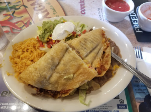 A plate of Mexican food featuring two crispy tacos, rice, beans, lettuce, tomato, guacamole, and sour cream.